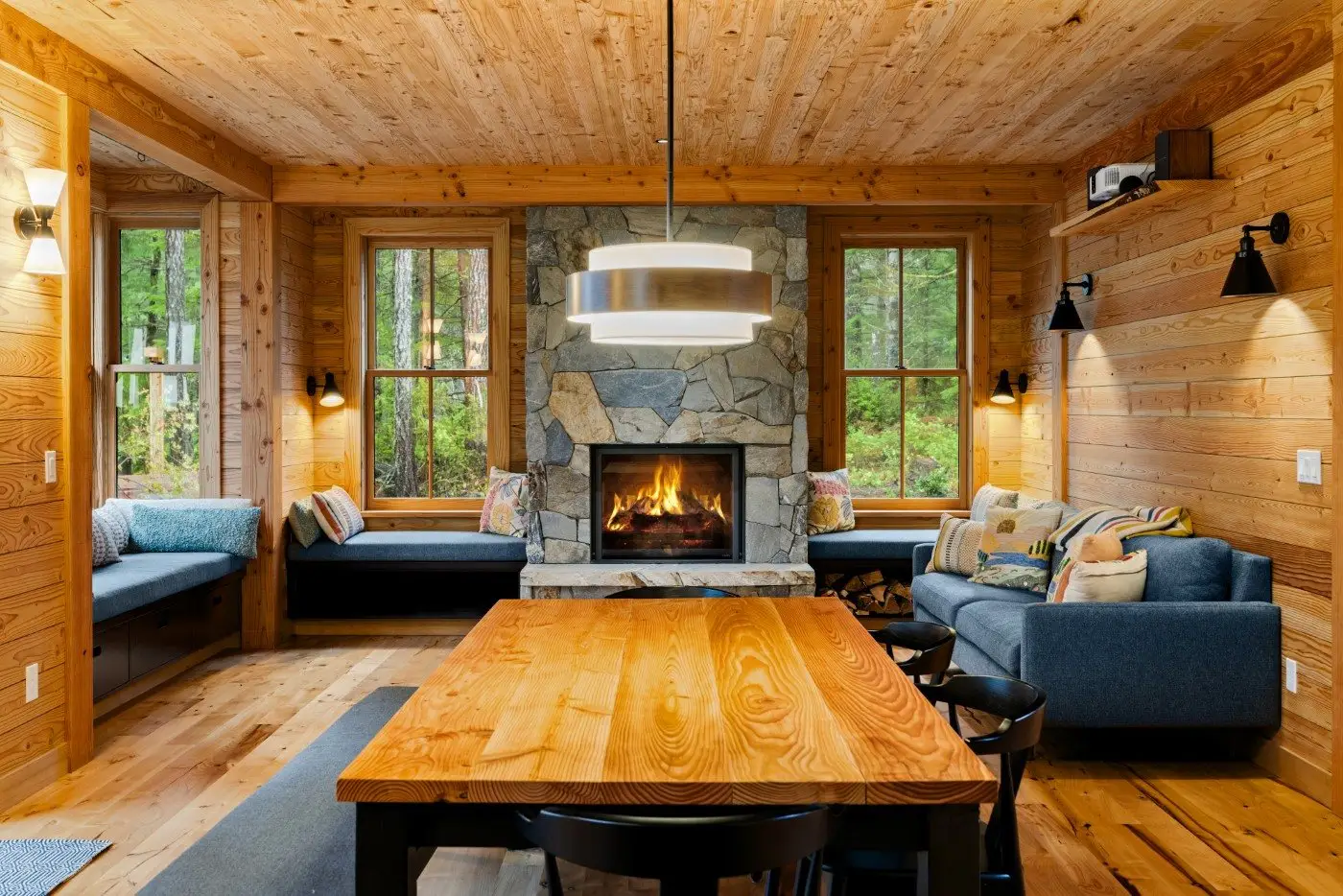 Wood-paneled cabin living room with a stone fireplace and a lit fire, built by Doyle Construction