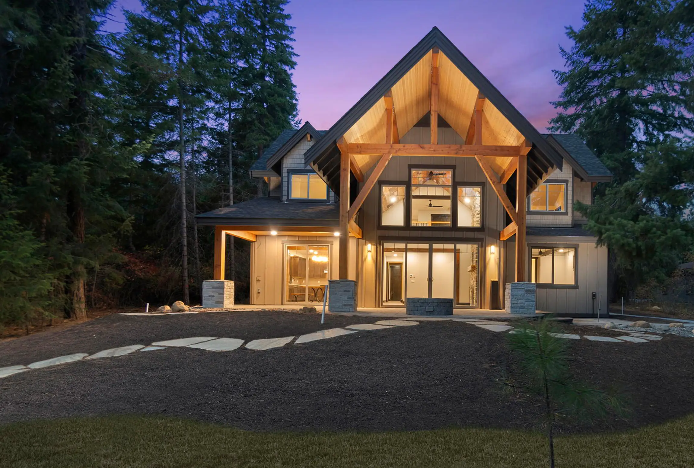 Modern A-frame custom home with large windows among tall evergreens