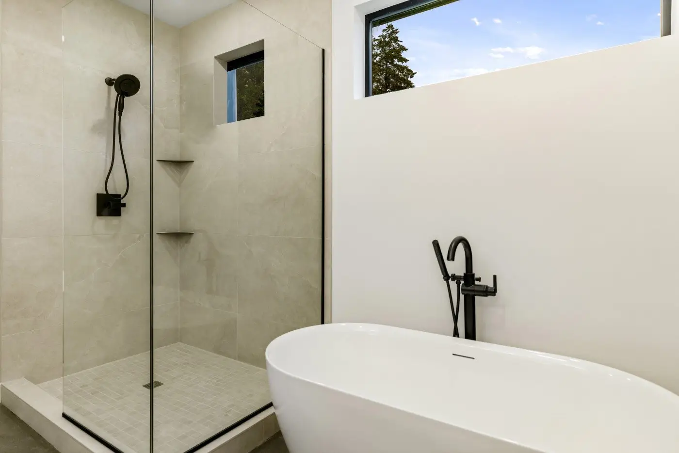 Modern bathroom with a glass-enclosed shower featuring a black rainfall showerhead, a freestanding white bathtub, and two rectangular windows letting in natural light. The decor is minimalist with neutral tones.