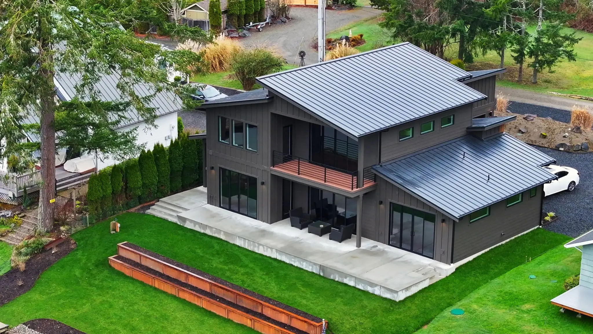 Aerial view of the Spencer Lake Custom home with shed roofs, patio, and lakeside lawn