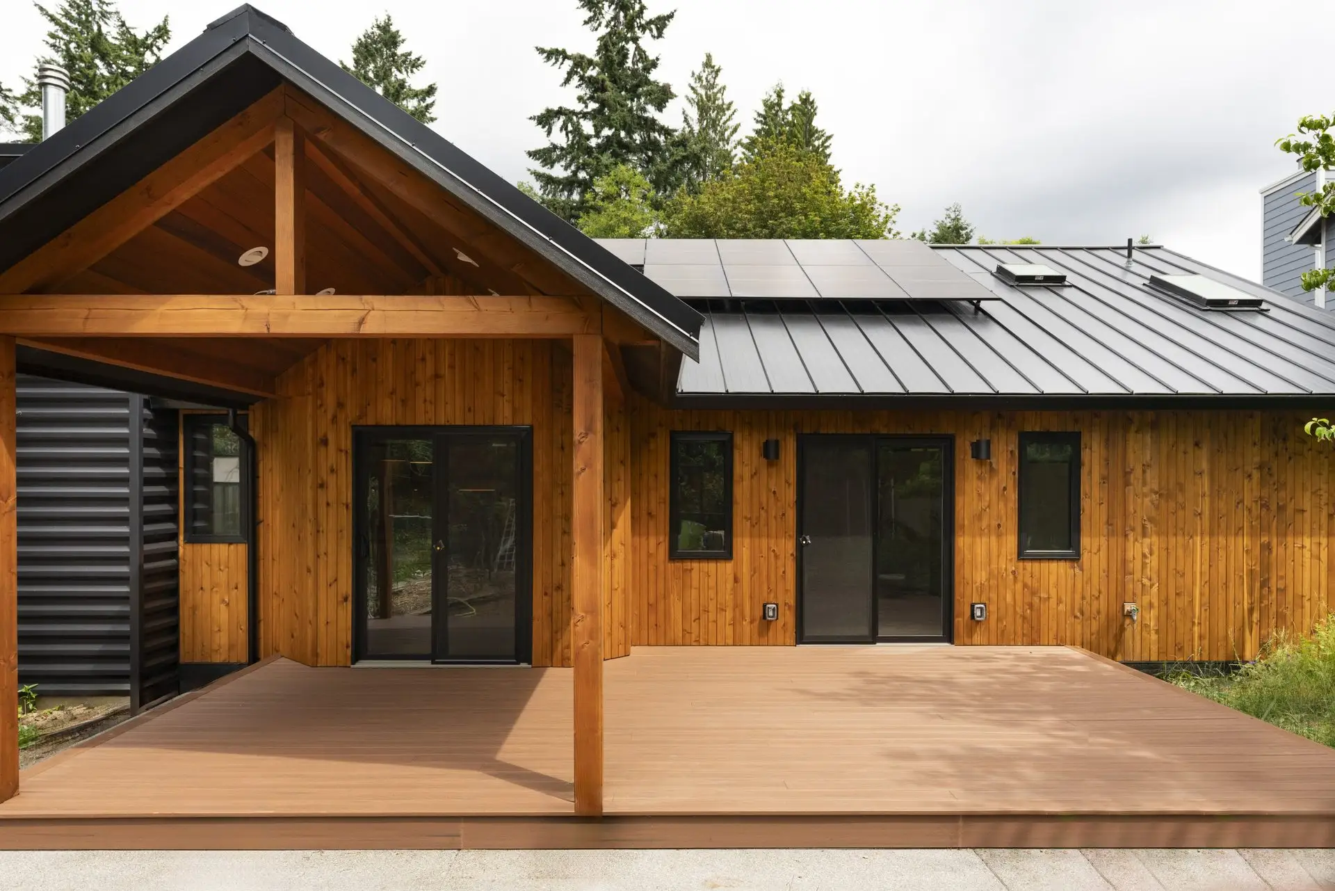 Covered back porch of the Westside Olympia Remodel with exposed timber posts, cedar siding, black-framed doors, and a wide composite deck